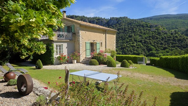 Una casa con balcón, cancha de tenis y montañas al fondo.
