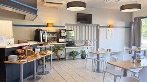 Un café moderno con estación autoservicio para bebidas, zona de estar y mostrador con alimentos.