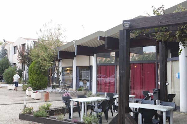 Un área de estar al aire libre con mesas y sillas, una sección cubierta y un edificio al fondo.