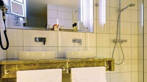 Un baño con ducha, dos lavamanos, un espejo y un secador de pelo.
