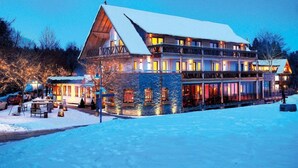 Un hotel de varios pisos con tejado cubierto de nieve, zona de estar al aire libre y ventanas iluminadas.