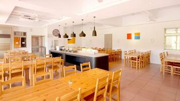 A spacious dining area with multiple wooden tables and chairs, a central island with a sink, and pendant lighting.