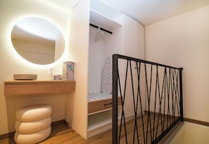 Ein Schlafzimmer mit einem hölzernen Schminktisch, einem runden Spiegel, einem Bett mit geometrischem Kopfteil und einem schwarzen Metallgeländer.