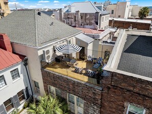 A rooftop terrace with outdoor furniture, a striped umbrella, and a view of the cityscape. - The Conroy | Perfect Location | Historic Charm (Charleston)