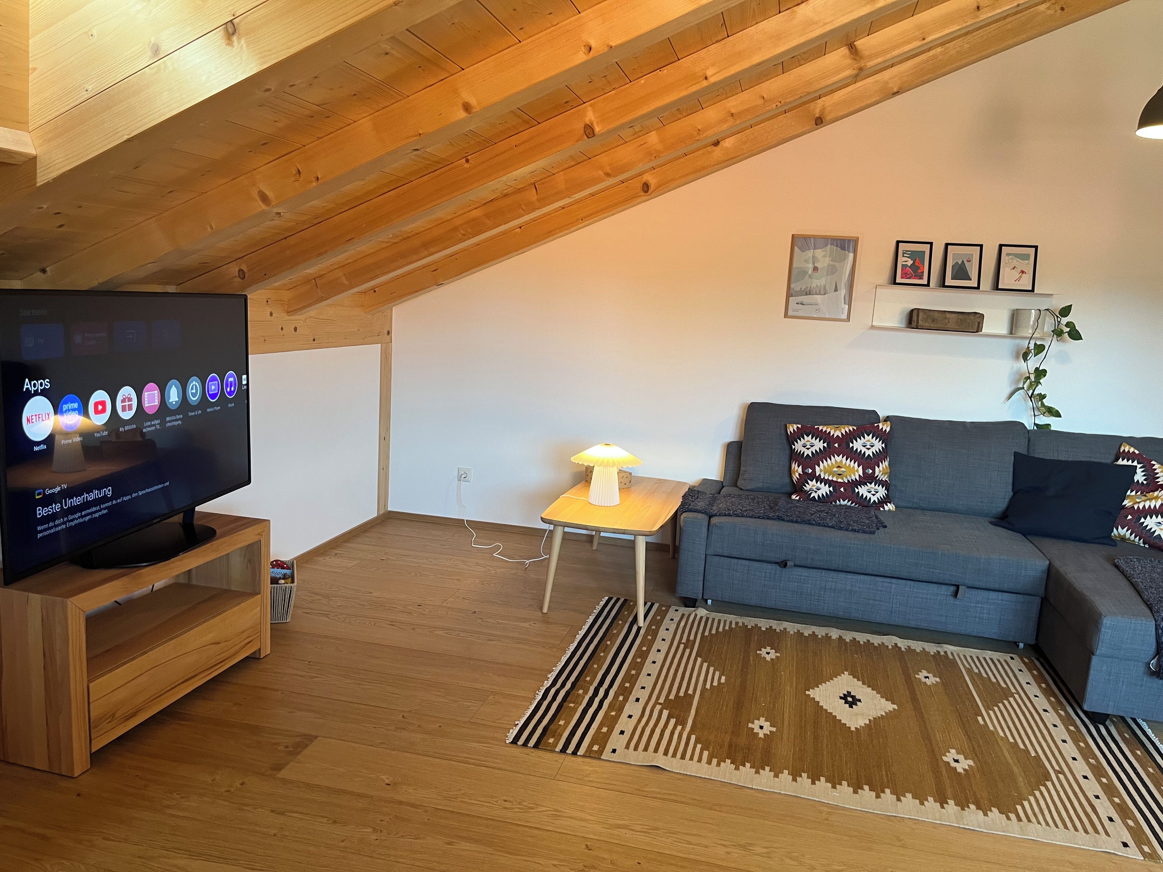 Ein Wohnzimmer mit Fernseher, auf dem App-Symbole angezeigt werden, einer Couch, einer Lampe und einem gemusterten Teppich.