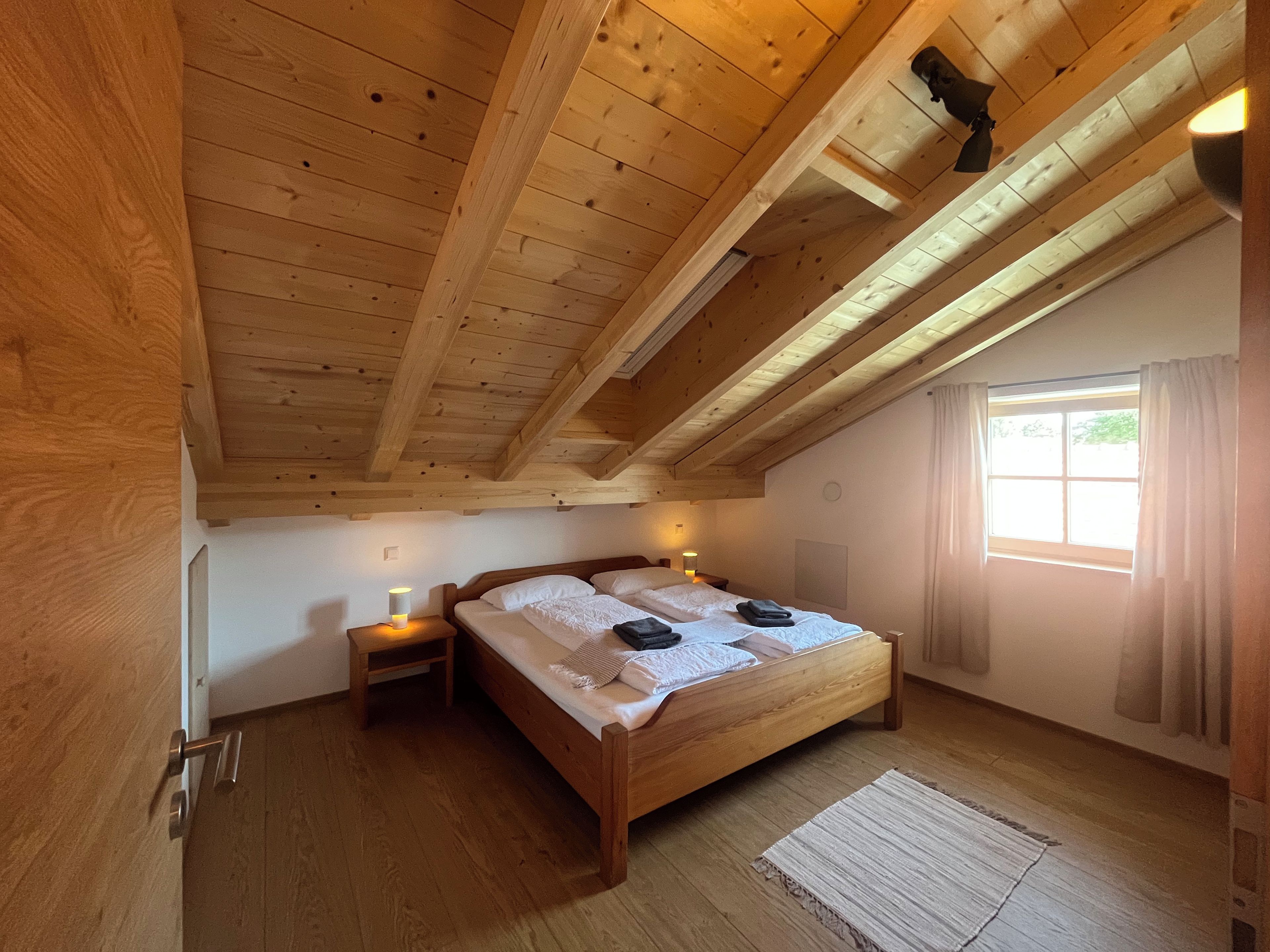 Ein Schlafzimmer mit Holzboden, einem Bett mit weißer Bettwäsche, zwei Nachttischen mit Lampen und einem Fenster mit Vorhängen.