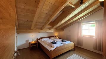 Ein Schlafzimmer mit Holzboden, einem Bett mit weißer Bettwäsche, zwei Nachttischen mit Lampen und einem Fenster mit Vorhängen.