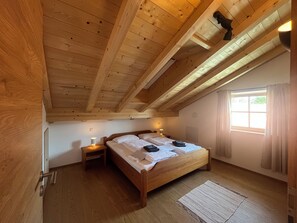 Ein Schlafzimmer mit Holzboden, einem Bett mit weißer Bettwäsche, zwei Nachttischen mit Lampen und einem Fenster mit Vorhängen.