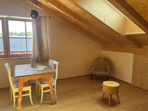 Ein Essbereich mit Tisch, Stühlen und einem kleinen Hocker, sowie ein Fenster mit Vorhängen.