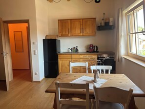 Eine Küche mit Holzausstattung, einem schwarzen Kühlschrank, einem Esstisch mit Stühlen und einem Fenster mit Vorhängen.