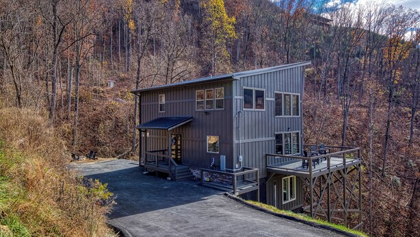A modern two-story building with a deck and a covered porch, surrounded by a forested area. - Indoor Pool, Mountain Views, 20-Ft Fireplace, Secluded, Hot Tub, Sleeps 12 (Gatlinburg)