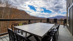 An outdoor deck with a wooden table and chairs, overlooking a forested hillside. - Indoor Pool, Mountain Views, 20-Ft Fireplace, Secluded, Hot Tub, Sleeps 12 (Gatlinburg)
