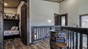 A rustic interior with a loft bed, a wooden railing, and a barrel stool. - Indoor Pool, Mountain Views, 20-Ft Fireplace, Secluded, Hot Tub, Sleeps 12 (Gatlinburg)