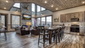 A spacious kitchen with modern appliances, a dining area with a high table and chairs, and a cozy seating area with a fireplace. - Indoor Pool, Mountain Views, 20-Ft Fireplace, Secluded, Hot Tub, Sleeps 12 (Gatlinburg)