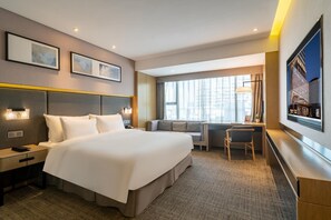 A hotel room with a large bed, a desk, and a chair. There are two framed pictures on the wall, a window with curtains, and a large TV screen. - Xiamen United Hotel (Xiamen)