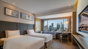 A hotel room with two beds, a desk, a chair, a large window with a city view, and framed artwork on the wall. - Xiamen United Hotel (Xiamen)