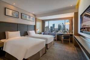 A hotel room with two beds, a desk, a chair, a large window with a city view, and framed artwork on the wall. - Xiamen United Hotel (Xiamen)