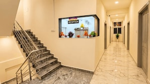 A hotel reception area with a marble staircase, a reception desk, and a hallway leading to elevators. - HOTEL STAY BLISS - HSR LAYOUT (Bengaluru)