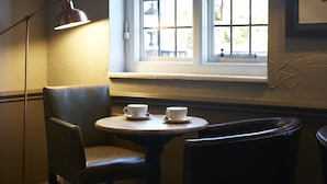 A corner seating area with a table and two chairs, a lamp, and a window with a view of the outside. - St Leonards (Ringwood)