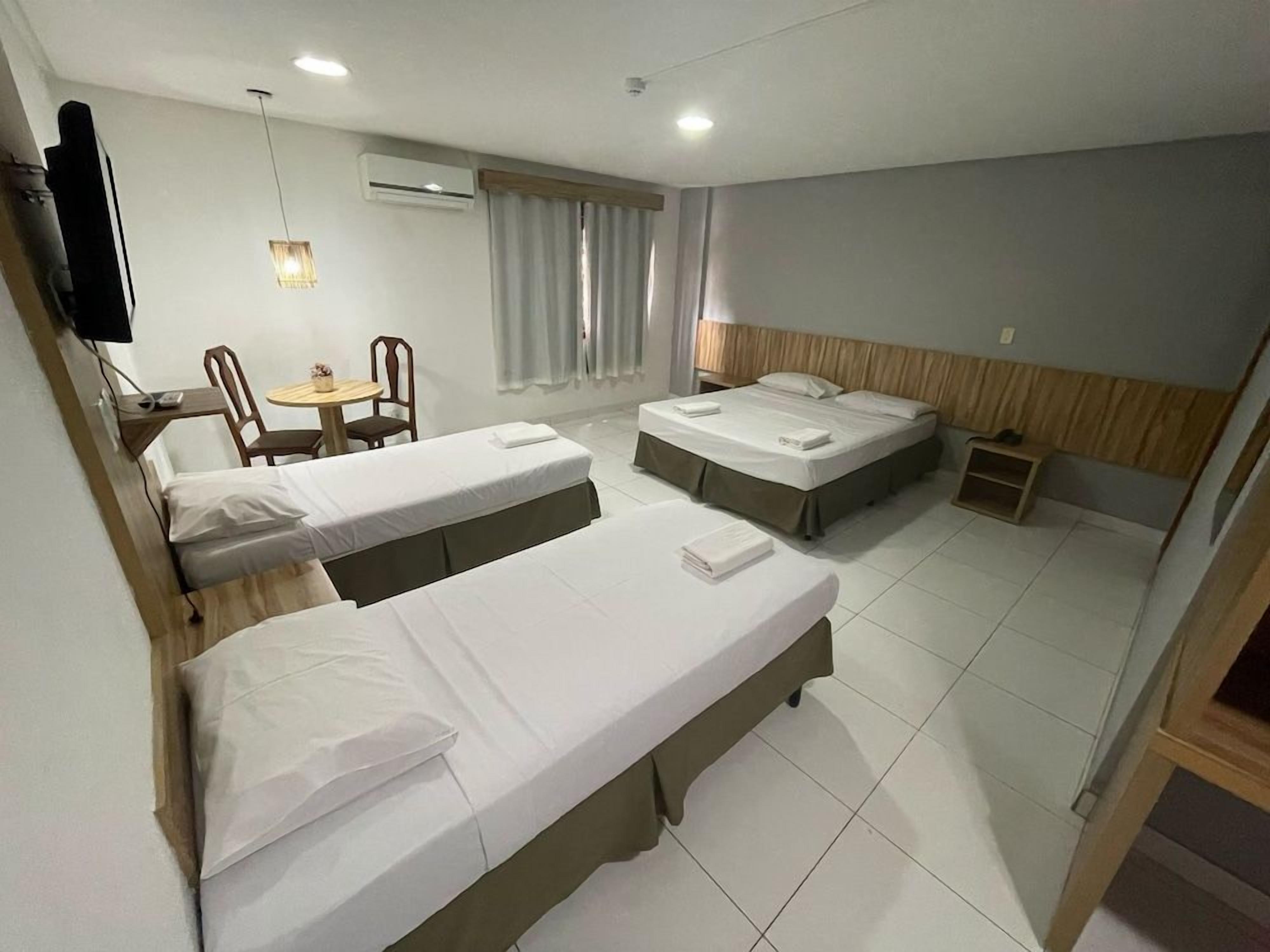Une chambre d’hôtel avec deux lits simples, une petite table avec des chaises, un téléviseur fixé au mur et un appareil de climatisation.
