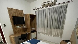 A hotel room with a bed, a desk, a chair, an air conditioning unit, and a television. - Pousada Serras De Goyaz (Goiânia)