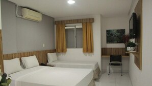 A hotel room with two beds, a desk, a chair, an air conditioning unit, a window with curtains, and a television. - Pousada Serras De Goyaz (Goiânia)