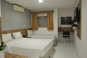 A hotel room with two beds, a desk, a chair, an air conditioning unit, a window with curtains, and a television. - Pousada Serras De Goyaz (Goiânia)