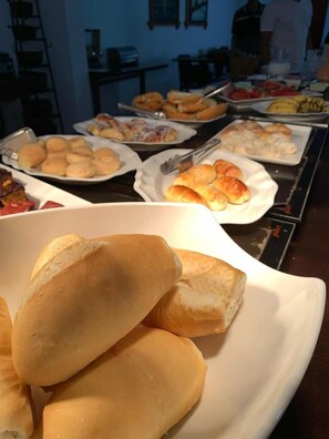 A buffet table with various food items including bread rolls and pastries. - Pousada Serras De Goyaz (Goiânia)