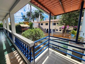A covered balcony with a view of a residential area, including a building with a red roof and a staircase. - Pousada Serras De Goyaz (Goiânia)