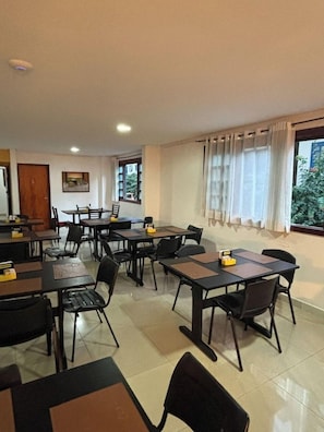 A conference room with multiple tables and chairs, a wooden door, and windows with curtains.