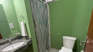 A bathroom with a green wall, a white toilet, a shower curtain, and a sink. - Pousada Serras De Goyaz (Goiânia)