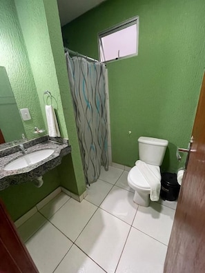 A bathroom with a green wall, a white toilet, a shower curtain, and a sink. - Pousada Serras De Goyaz (Goiânia)