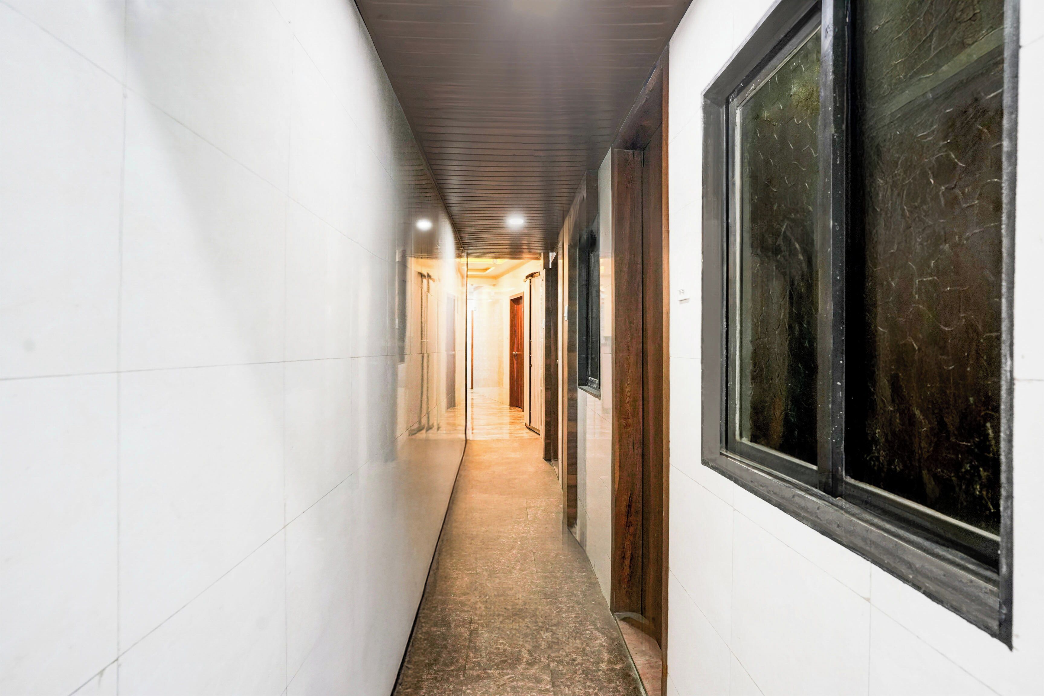 A narrow hallway with white walls and a tiled floor, leading to a door at the end.