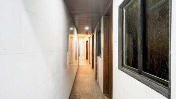 A narrow hallway with white walls and a tiled floor, leading to a door at the end.