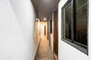 A narrow hallway with white walls and a tiled floor, leading to a door at the end.