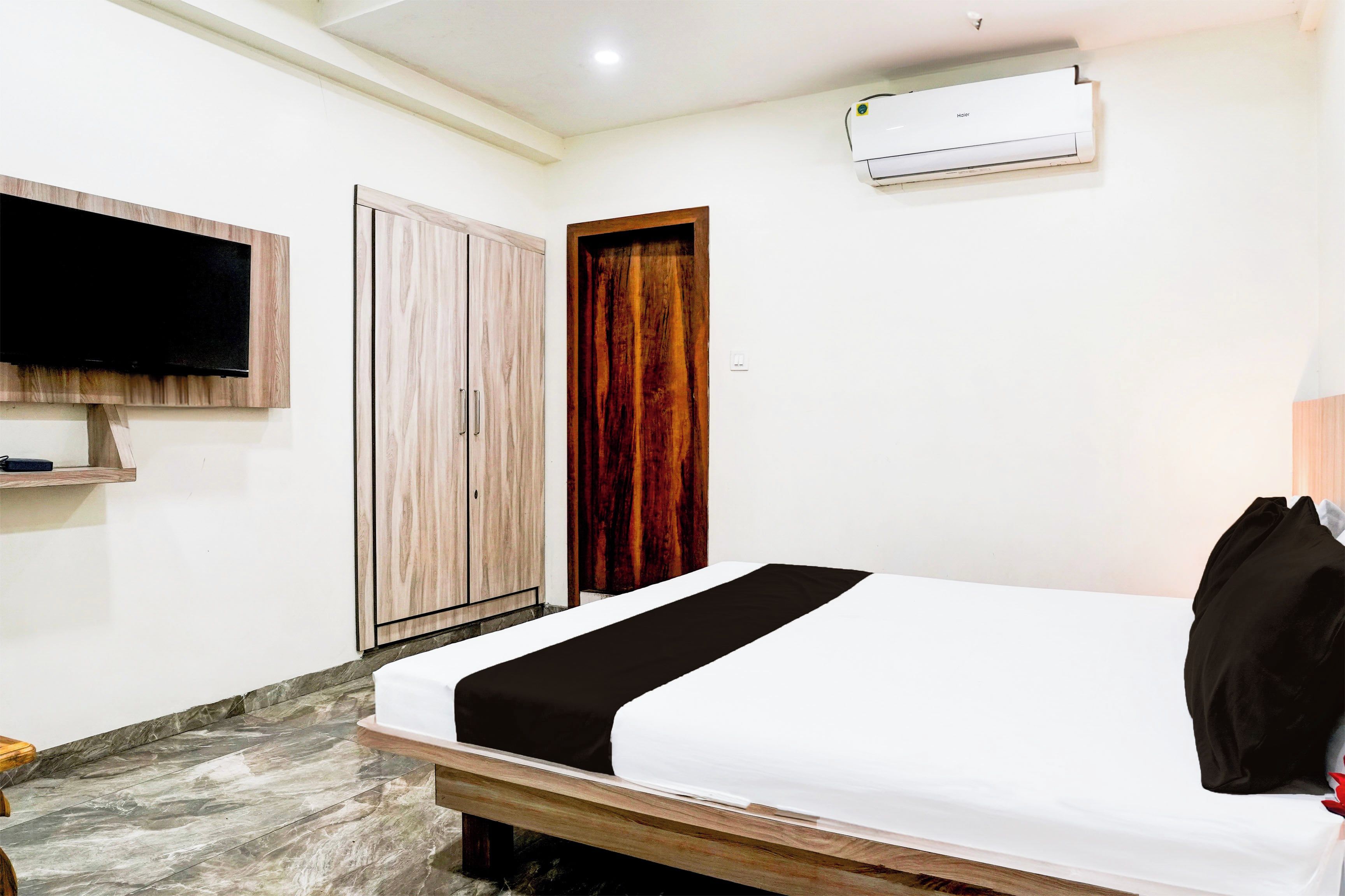 Una habitación de hotel con una cama, un televisor montado en la pared, un armario y un equipo de aire acondicionado.