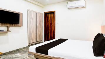 Una habitación de hotel con una cama, un televisor montado en la pared, un armario y un equipo de aire acondicionado.