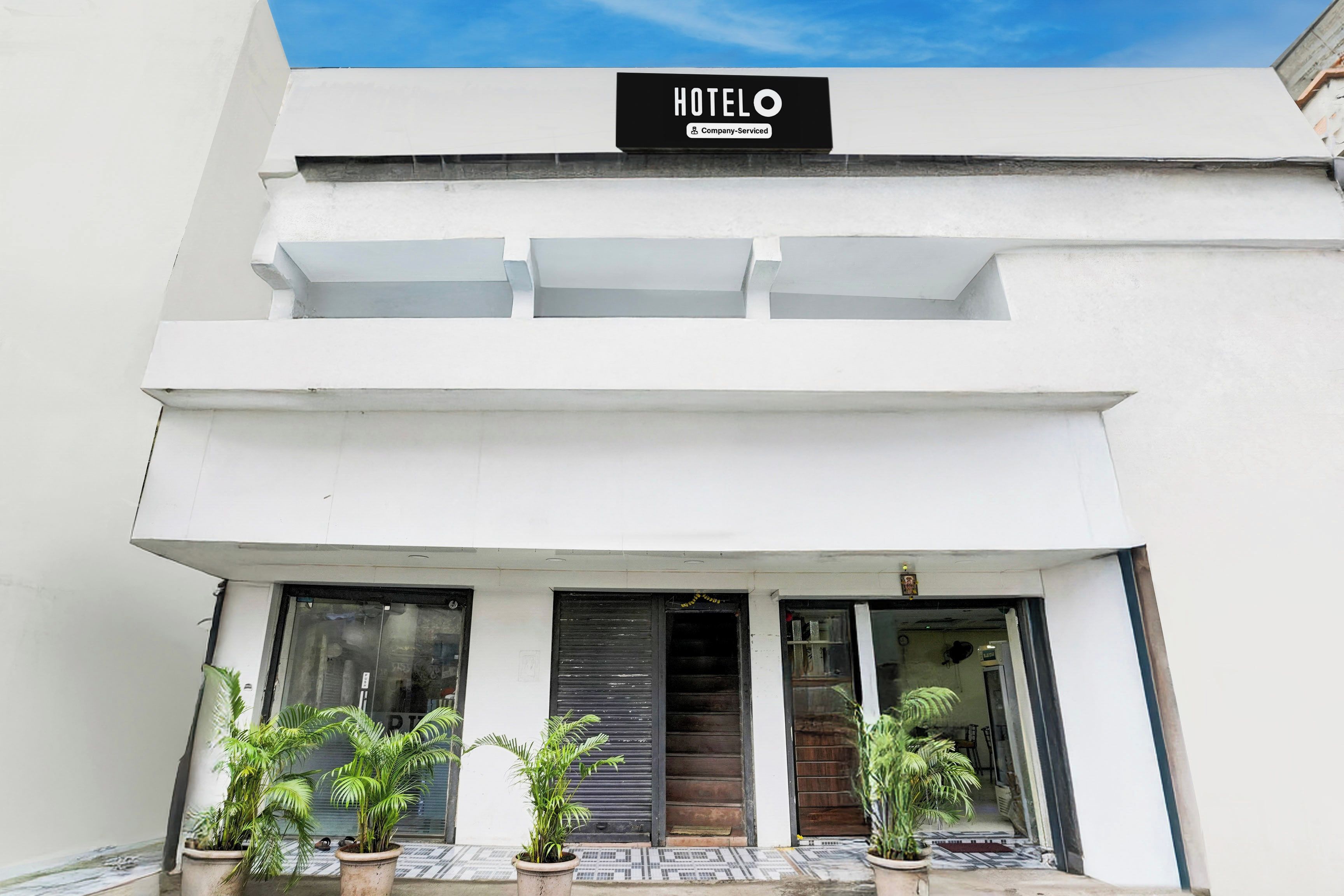 A modern hotel with a sign indicating it is company-serviced. There are two potted plants in front of the entrance.