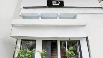 A modern hotel with a sign indicating it is company-serviced. There are two potted plants in front of the entrance.