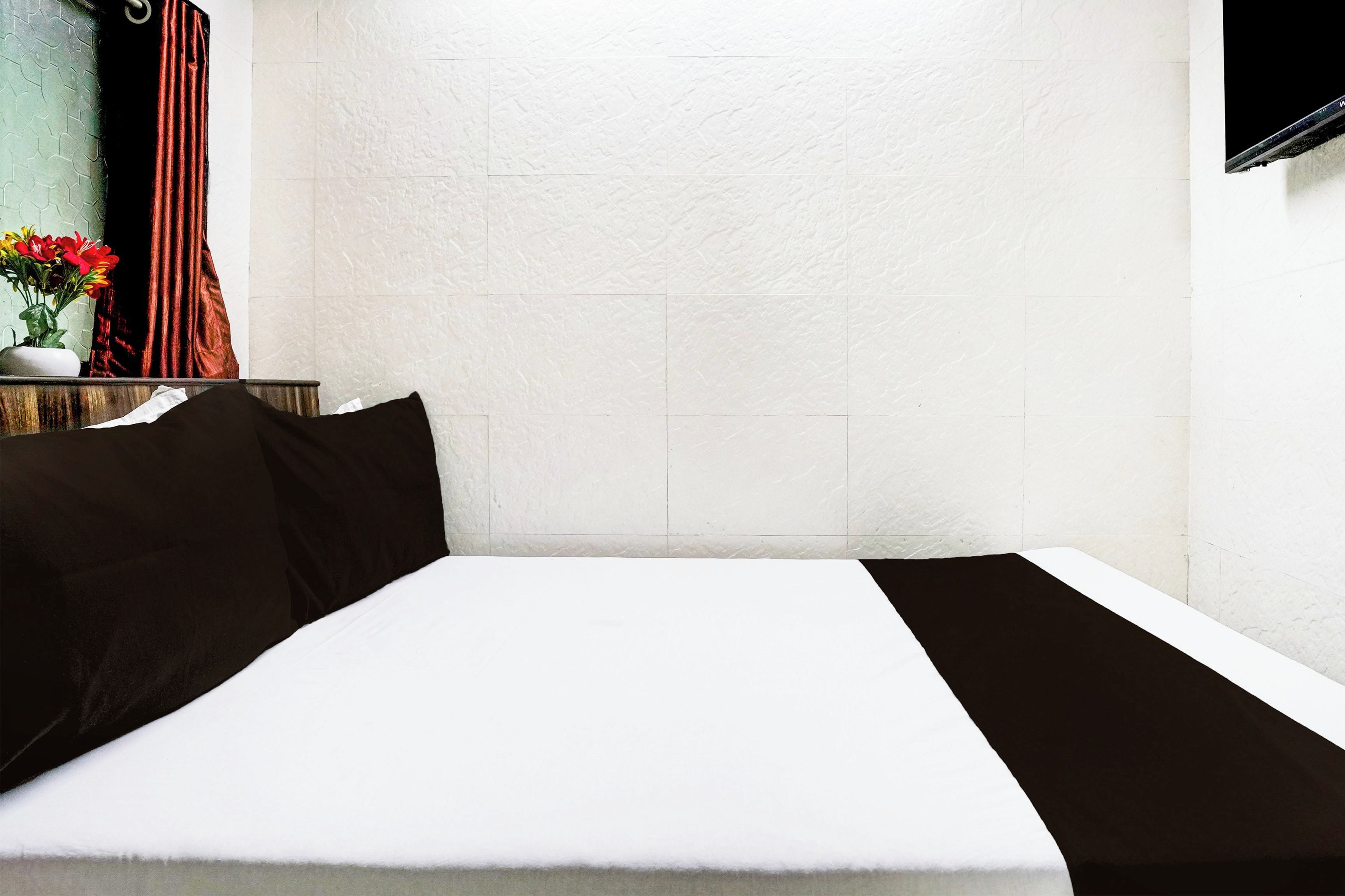 A hotel room with a bed, a nightstand, a vase with flowers, and a wall-mounted TV.
