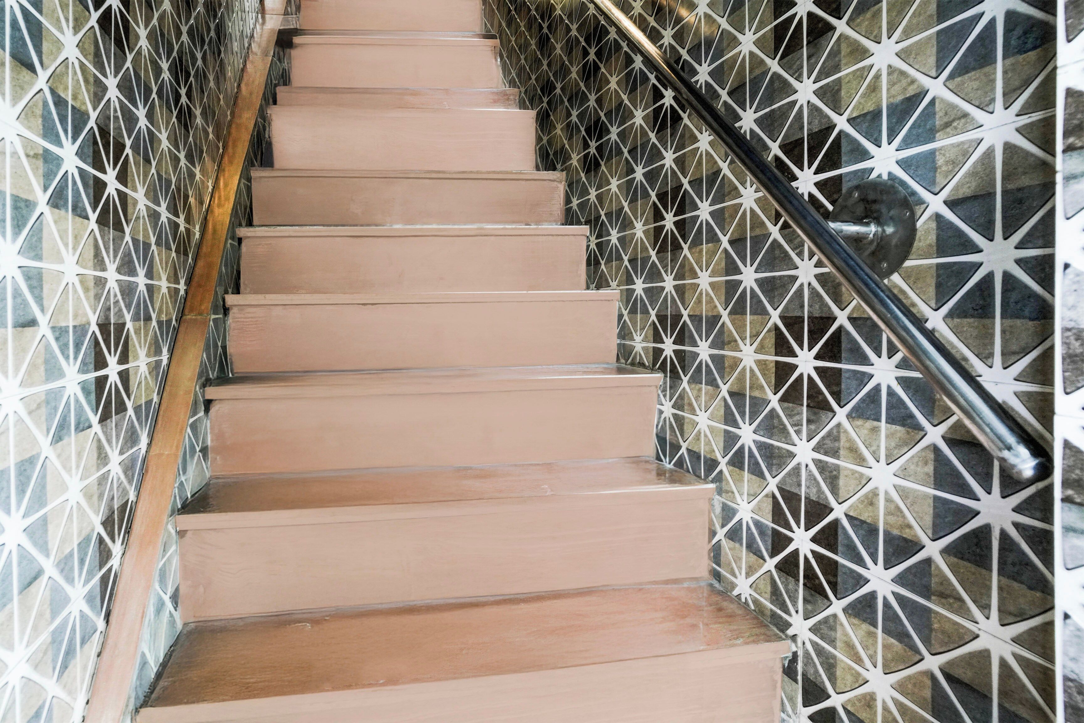 Una escalera con un revestimiento mural de diseño geométrico y una barandilla de metal.