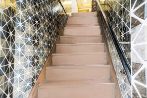 Una escalera con barandilla de diseño geométrico y pared lisa.