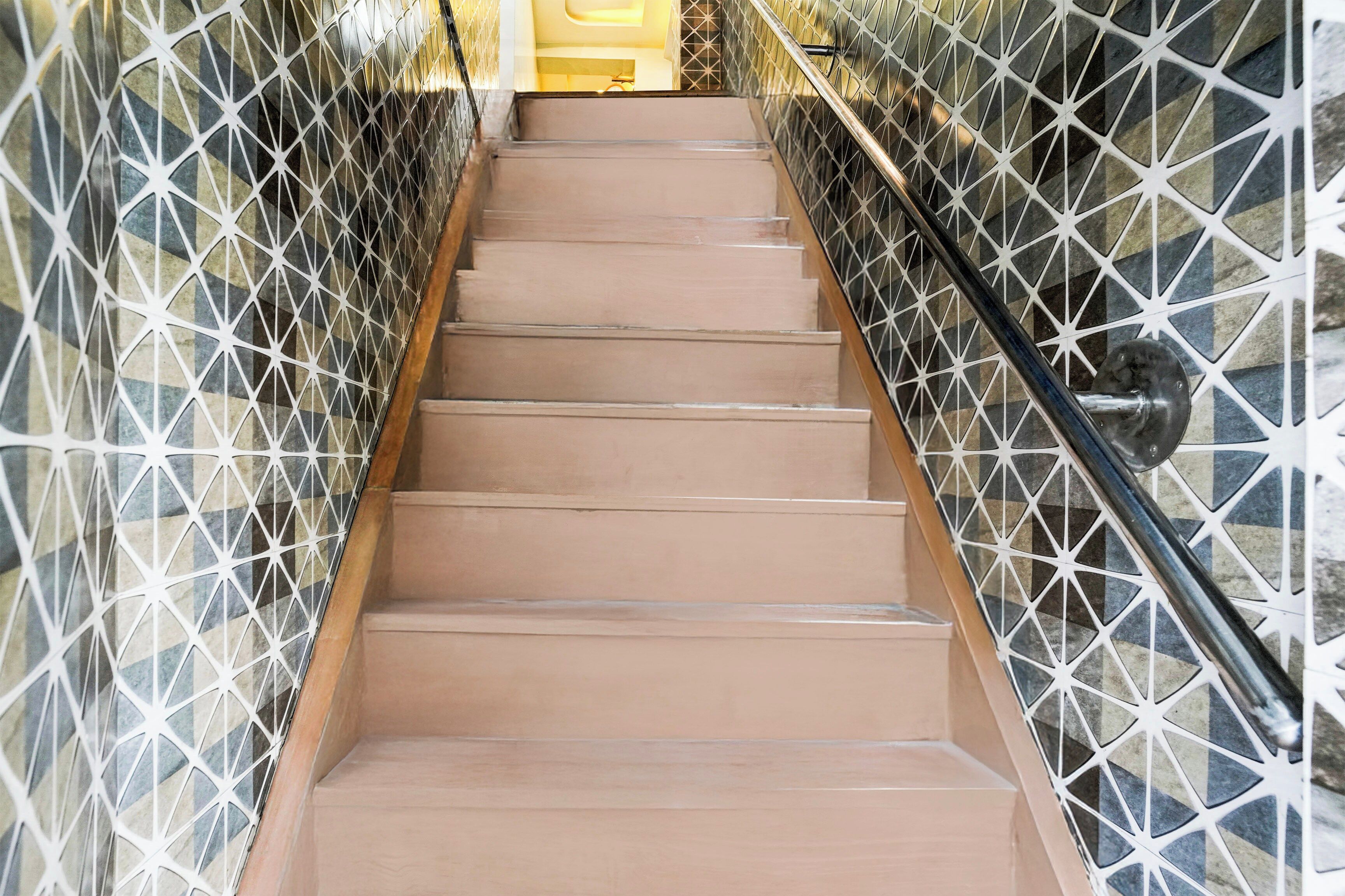 Una escalera con paredes laterales de diseño geométrico y una barandilla metálica.
