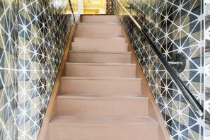 Una escalera con paredes laterales de diseño geométrico y una barandilla metálica.