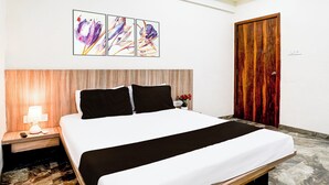 A hotel room with a bed, a nightstand with a lamp, a wooden headboard, a wooden door, and a wall with three framed pictures. - Hotel O Dombivali Formerly PK Lodging (Kalyan)