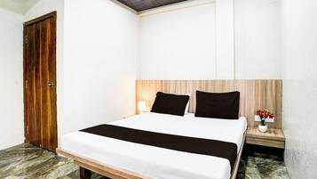 A hotel room with a bed, a wooden headboard, a nightstand with a lamp, and a small table with a vase of flowers.