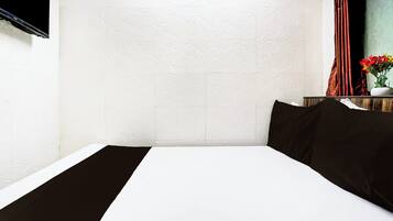 Una habitación de hotel con una cama, una ventana con cortinas y un florero con flores sobre una mesita de noche.