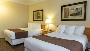 A hotel room with two beds, a nightstand with a lamp, and two framed pictures on the wall. - Bcm Inns Fort Mcmurray - Downtown (Fort McMurray)