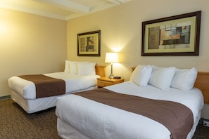 Una habitación de hotel con dos camas, una mesita de noche con lámpara y dos cuadros en la pared.