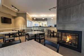 A restaurant with multiple tables and chairs, a flat-screen TV mounted on the wall, and a fireplace with a visible fire.